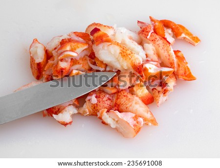 A portion of cut cooked lobster meat on a plastic cutting board with a kitchen knife.