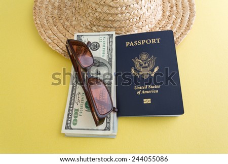 A passport next to vacation money with sunglasses on a yellow background with a straw hat in the background.