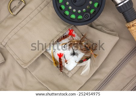 A group of assorted fly fishing flies on a vest with a cork handle fly rod and reel.