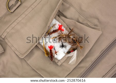 A group of assorted fly fishing flies on the fleece patch of a fishing vest.