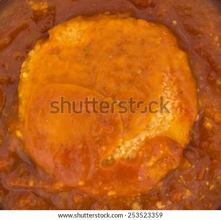 A very close view of a chicken parmagiana patty in tomato sauce.