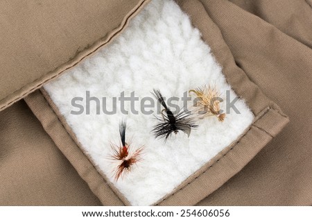 A very close view of three very small fly fishing flies on the fleece patch of a fishing vest.