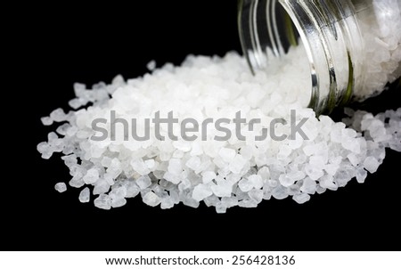 A glass container of sea salt on its side spilling on to a black background.