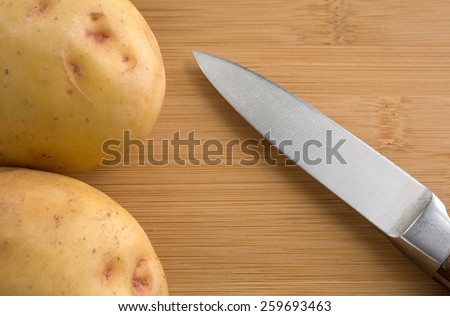 Close view of two yellow gold potatoes on a wood cutting board with a sharp knife.