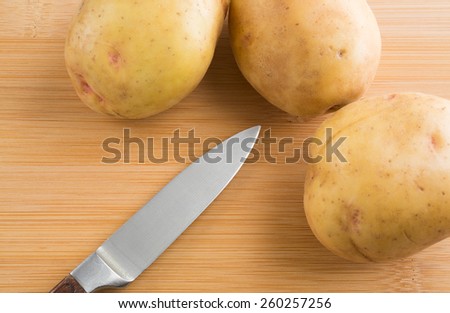 A group of yellow gold potatoes on a wood cutting board with a sharp knife.
