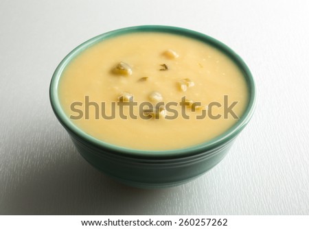 A bowl of cream of celery soup on a white cutting board illuminated by window light.