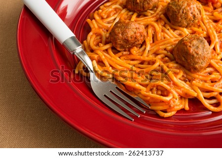 A spaghetti and meatball TV dinner on a red plate with a fork on a tan table cloth.