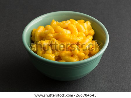 A small bowl of macaroni and cheese on a dark background illuminated by window light.