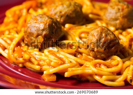 A very close view of a spaghetti and meatball TV dinner on a red plate.