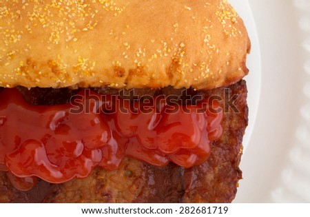 A very close view of a pork rib sandwich with ketchup added on a white paper plate.