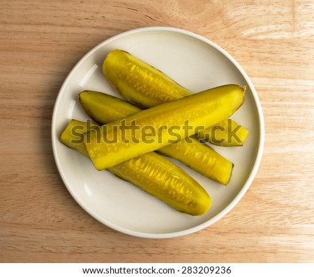 Top view of several bread and butter pickle spears on a small plate atop a wood table top illuminated by window light.