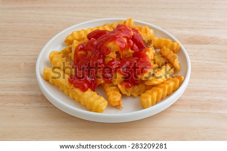 Crispy French fries covered with ketchup in a small plate on a wood table top.