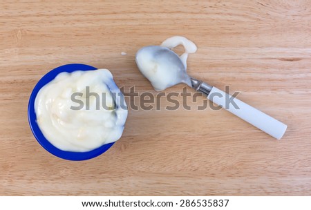 A small blue bowl with a serving of pineapple yogurt plus a white spoon to the side with a portion spilled on a wood table top.