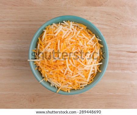 Top view of a small bowl filled with shredded white cheddar, sharp cheddar and mild cheddar cheeses atop a wood table top.