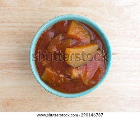 Top view of a small bowl filled with cooked zucchini in a tomato sauce on a wood table top illuminated by window light.
