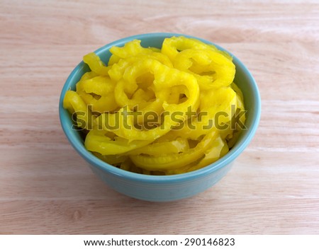A small bowl filled with crinkle cut banana peppers on a wood table top.