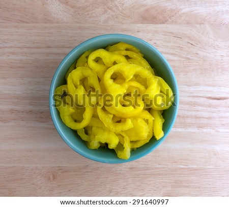Top view of a small bowl filled with crinkle cut banana peppers on a wood table top.