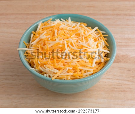 A small bowl filled with shredded white cheddar, sharp cheddar and mild cheddar cheeses atop a wood table top.