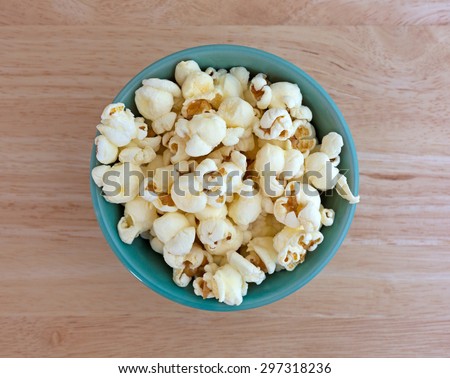Top view of a small bowl filled with a serving of white cheddar cheese flavored popcorn on a wood table top illuminated with natural light.