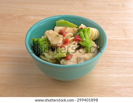 A small bowl with a serving of grilled chicken chunks and assorted vegetable in a garlic sauce atop a wood table top illuminated with natural light.