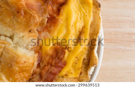Close top view of a bacon egg and cheese croissant breakfast sandwich on a small plate atop a wood table top illuminated with window light.