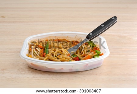 A TV dinner of noodles and vegetables in a white tray with a fork on a wood table top.