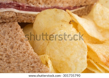 Close view of a roast beef wheat bread sandwich with white cheese and mayonnaise plus potato chips.