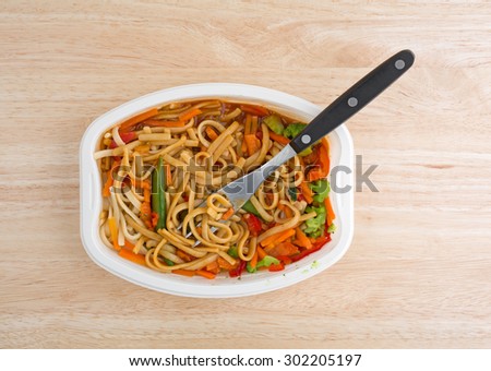 Top view of a TV dinner of noodles and vegetables in a white tray with a fork on a wood table top.