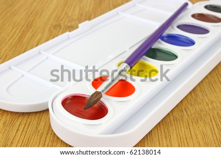 A close view of a new watercolor paint set with the brush on a wood background.