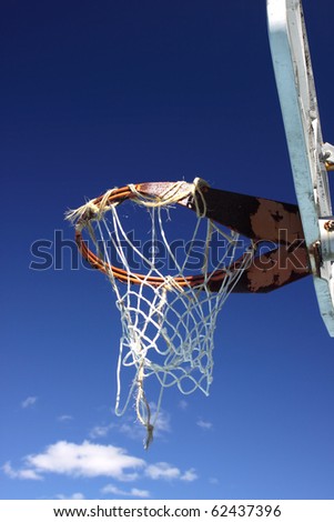 An old basketball hoop and net against a brilliant deep blue sky with wispy clouds.