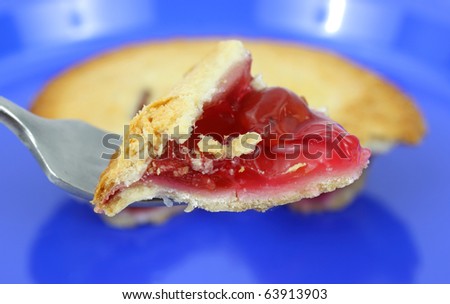A bite sized piece of cherry pie on a fork with blue plate in background.