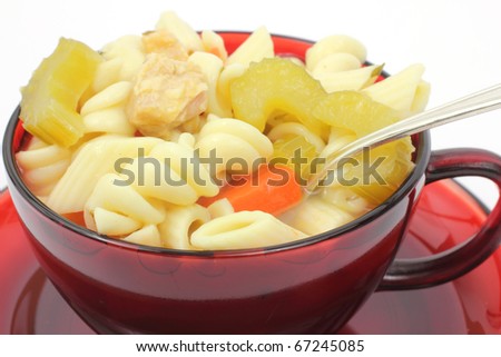 A red cup filled with chicken rotini pasta vegetable soup and a spoon on a white background.