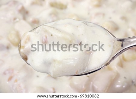 Spoon filled with clam chowder in the foreground with bowl filled in the background.