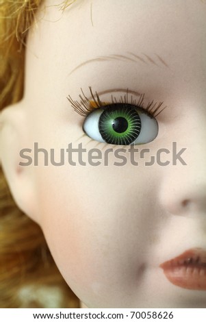 Part of an old doll\'s face showing half of nose, lips and green eye.