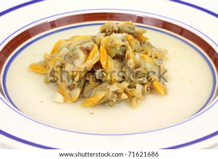 Close view of a plate with small clams in broth on a white background.