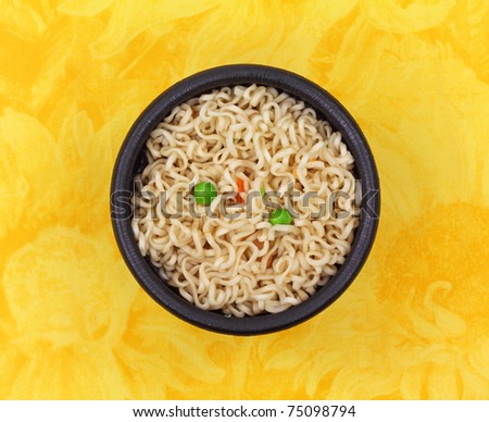 A serving of noodles peas and carrots in a black bowl on a yellow floral cloth background.