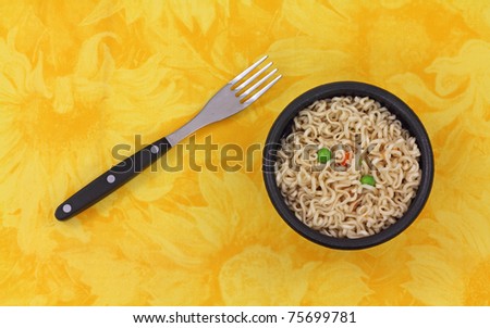 A serving of noodles in a black bowl with fork on a yellow floral cloth background.