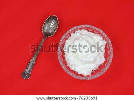 A serving of cottage cheese with spoon on red cloth background.