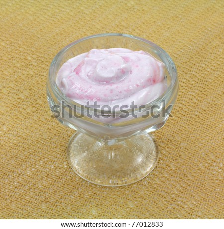 A small serving of pomegranate yogurt in glass dessert dish on a tan cloth background.