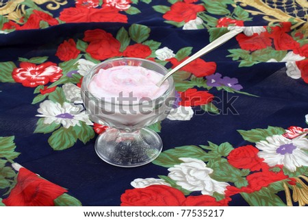 Pomegranate yogurt in dessert dish with spoon on a colorful floral cloth background.
