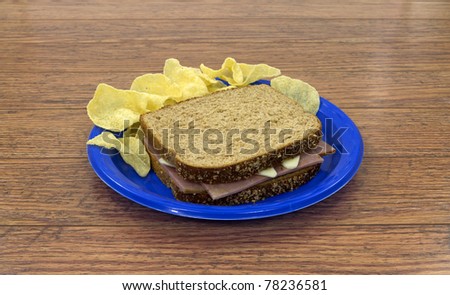 A turkey ham and cheese sandwich with potato chips on a blue plate.