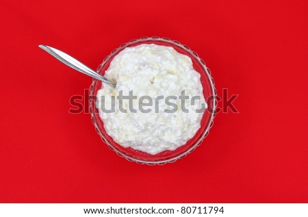 A single serving of pineapple cottage cheese with spoon in a glass dish on a red background.
