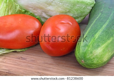 Close view of salad ingredients with lettuce tomatoes and cucumber on a wood cutting board.