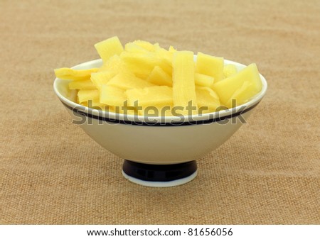 Sliced bamboo shoots in a small blue striped dish on burlap cloth background.