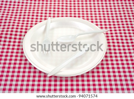 A foam picnic plate with plastic silverware on a checkerboard tablecloth.