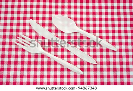A set of plastic silverware arranged on a red and white picnic tablecloth.