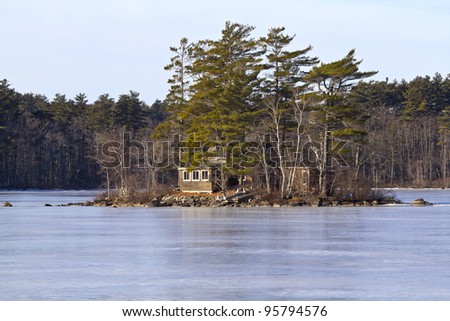 Close view of a rustic cabin on a small island surrounded by a lake that is iced over.