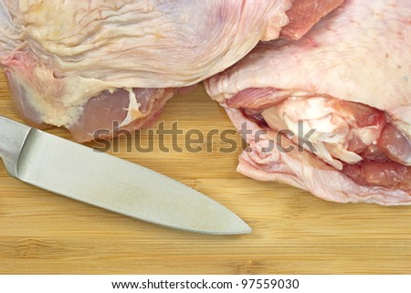 Close view of turkey thighs on a wood cutting board with knife blade.