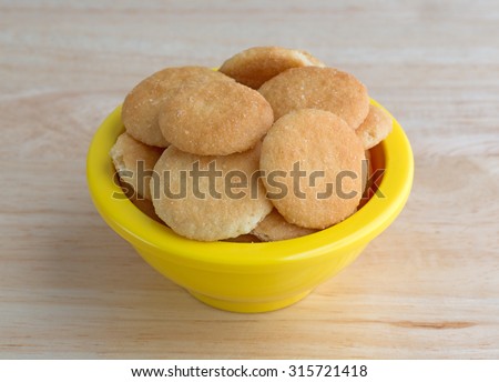 A small yellow bowl filled with vanilla flavored wafer cookies on a wood table top illuminated with natural light.