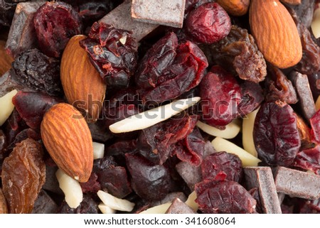 Close view of a trail mix consisting of dried cranberries, sliced almonds, raisins and chunks of chocolate illuminated with natural light.